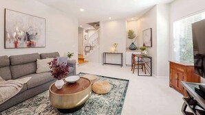 Un salon moderne avec un canapé, une table basse et un téléviseur. Un escalier mène à un autre niveau.