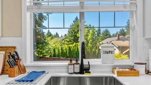 Une cuisine avec une fenêtre donnant sur l’extérieur, un évier en acier inoxydable, un bloc à couteaux et un bac à compost.