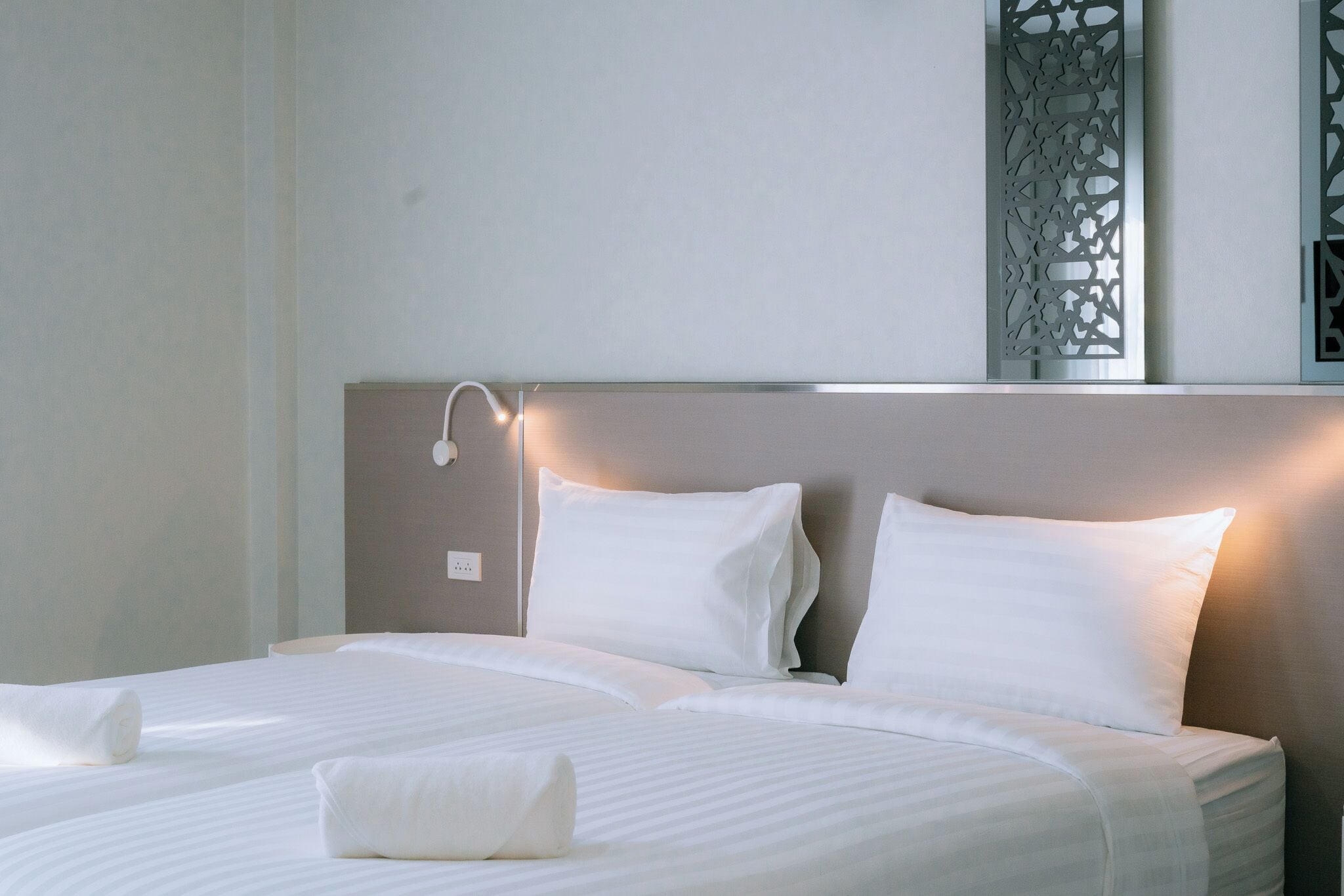 Een hotelkamer met een groot bed, twee kussens, een bedlampje en een decoratief wandpaneel.