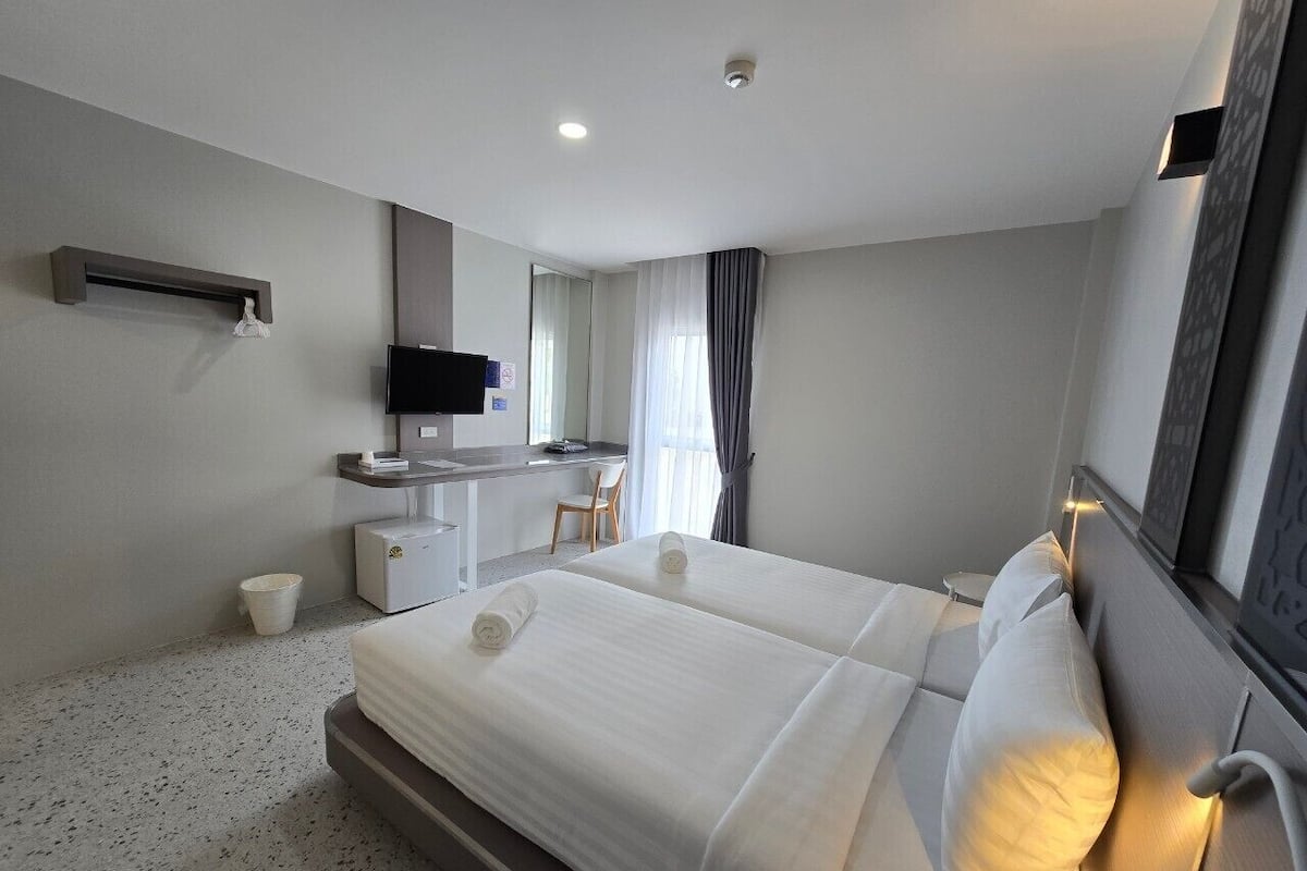 Una habitación de hotel con una cama grande, un escritorio con silla, un televisor y un ventanal con cortinas.