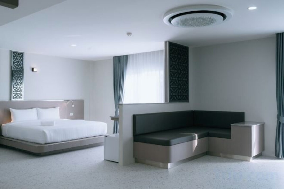 A modern hotel room with a bed, a seating area, and a large window.