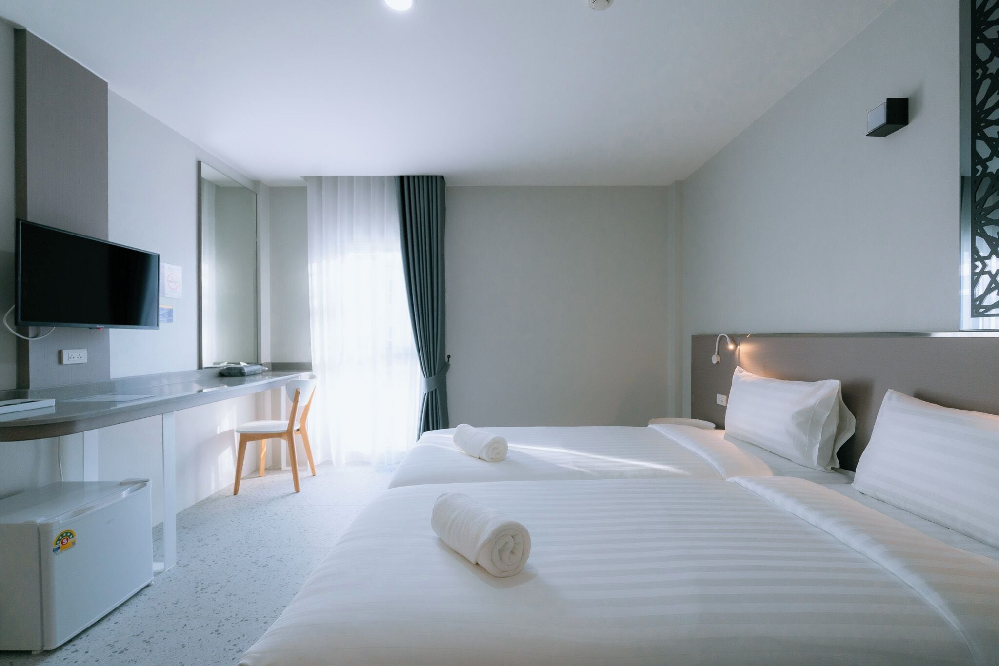 A hotel room with two beds, a desk, a chair, and a television.