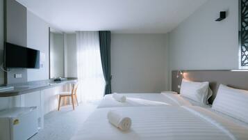 A hotel room with two beds, a desk, a chair, and a television.