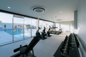 A gym with treadmills, dumbbells, and a pool visible through large windows. - One Budget Hotel Chiangrai Bypass-East (Chiang Rai)