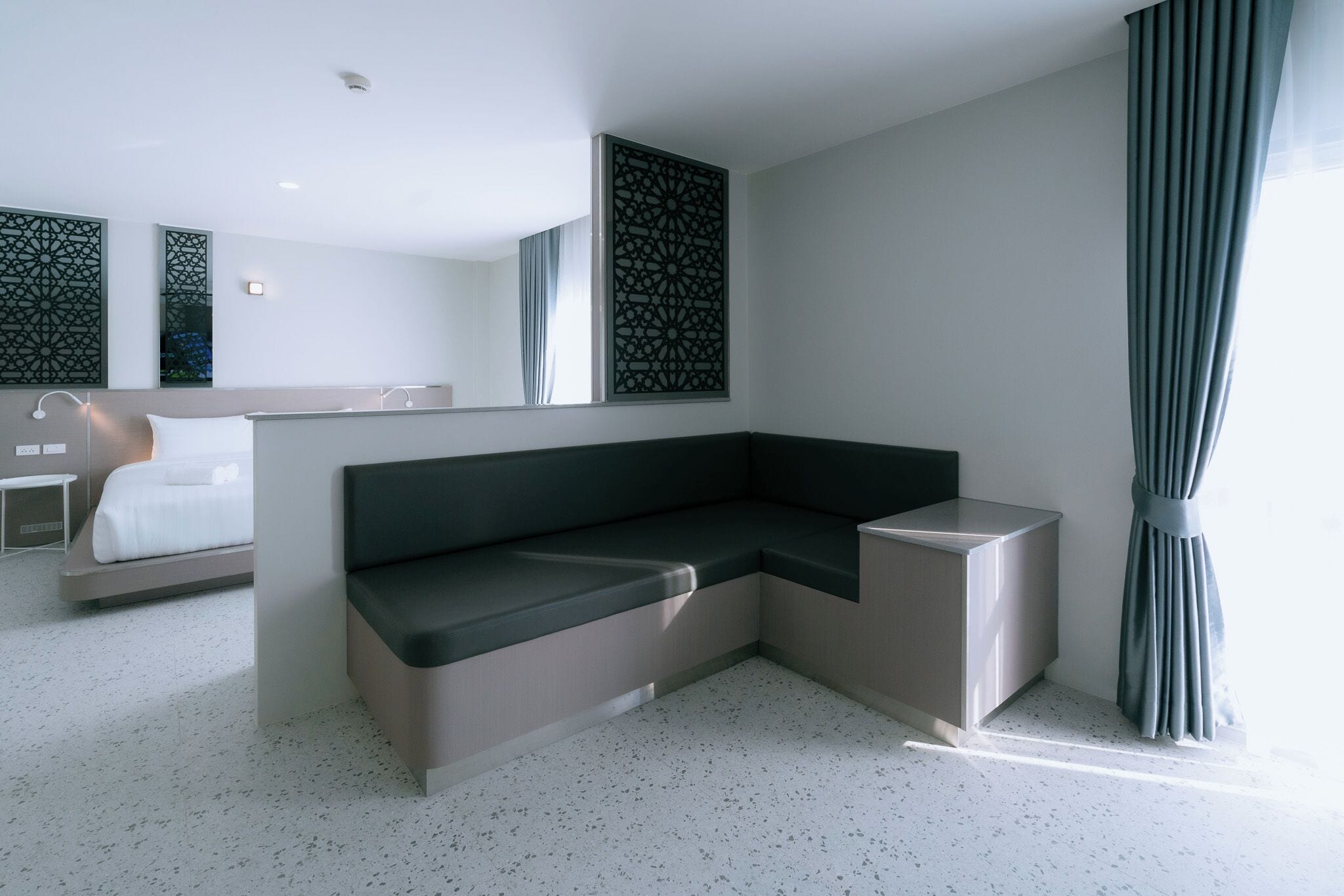 Een moderne hotelkamer met een hoekbed, een klein nachtkastje, een ingebouwde bank en een grote spiegel.