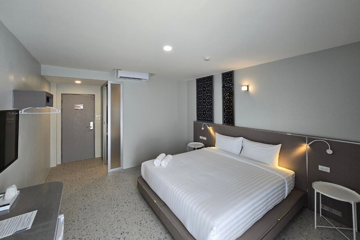 Una habitación de hotel con cama, mesitas de noche, un escritorio y televisión.