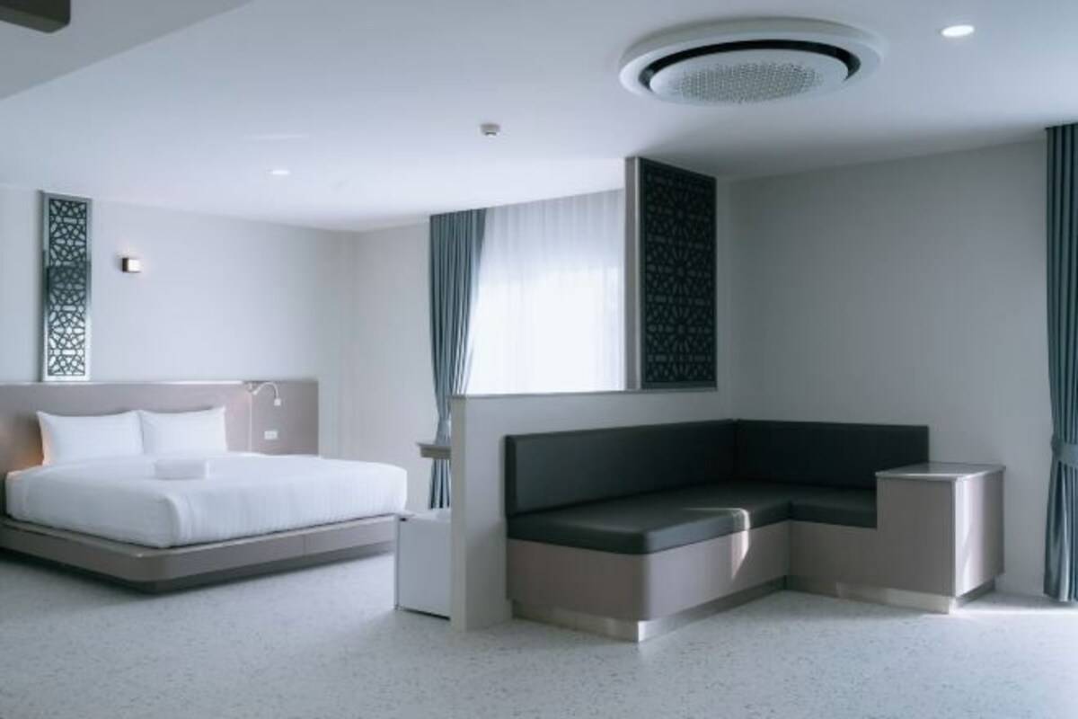A modern hotel room with a bed, a built-in bench, and a small bedside table.