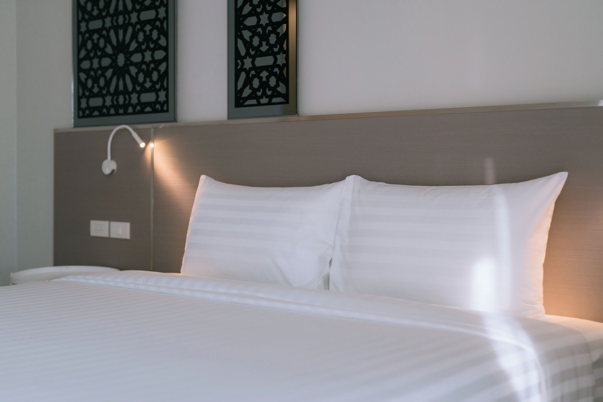 A neatly made bed with white linens, a headboard with a light fixture, and decorative wall panels.