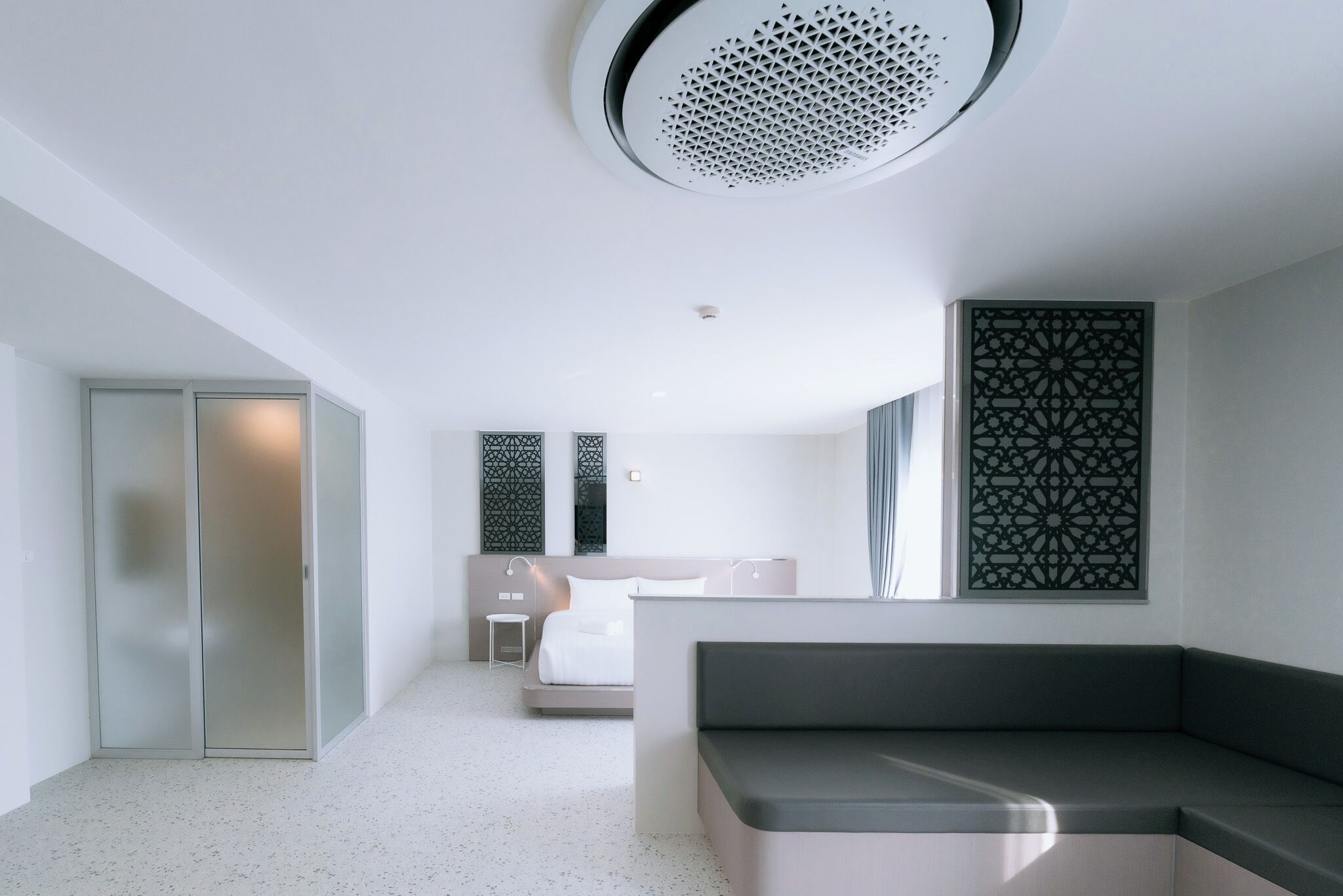 A modern hotel room with a kitchenette, a bed, a seating area, and a decorative wall panel.