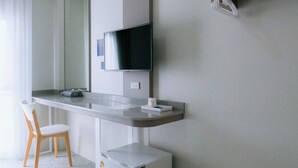 Une chambre d’hôtel moderne équipée d’un téléviseur à écran plat fixé au mur, d’un petit réfrigérateur, d’une poubelle blanche et d’une chaise en bois.