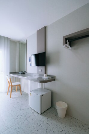 A modern hotel room with a flat-screen TV mounted on a wall, a small refrigerator, a white trash bin, and a wooden chair. - One Budget Hotel Chiangrai Bypass-East (Chiang Rai)