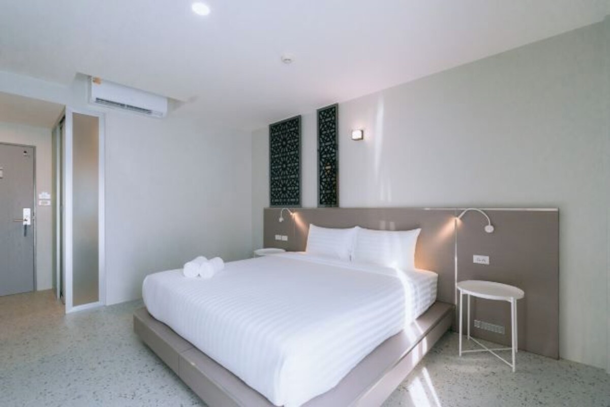A modern hotel room with a large bed, a bedside table, and a wall-mounted light fixture.