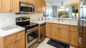 A kitchen with wooden cabinets, stainless steel appliances, and a large window providing a view of the outdoors.