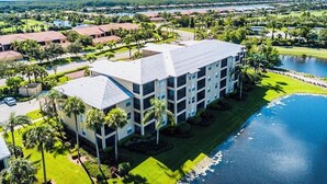 A multi-story hotel with a flat roof, surrounded by palm trees and a body of water.