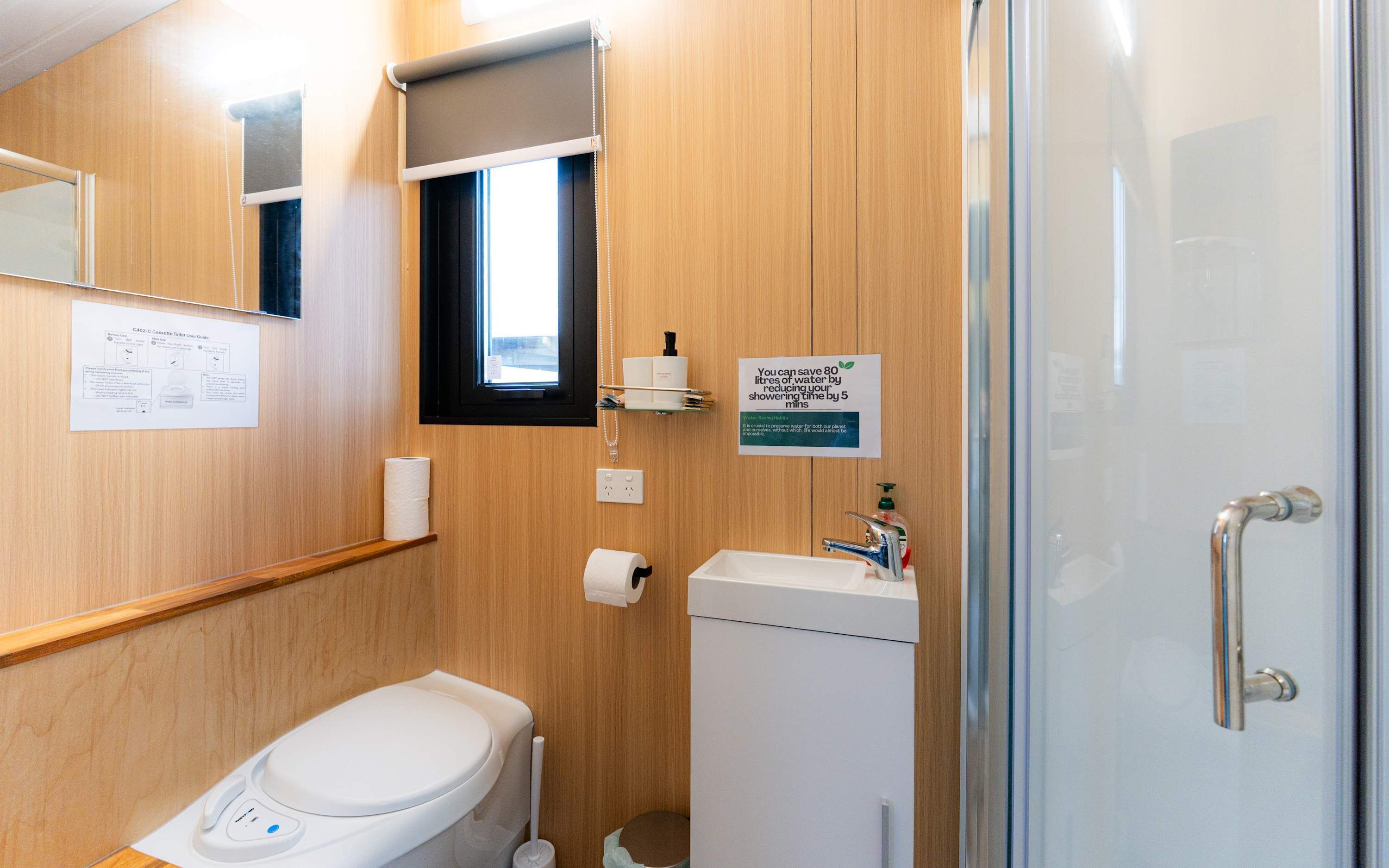 A modern bathroom with a toilet, sink, and shower. There is a sign indicating water savings.
