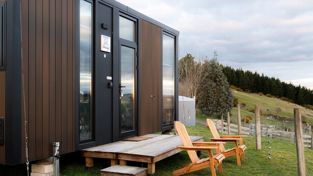 Una cabaña moderna con terraza de madera, dos sillas de madera y una mesa.