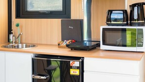 Une cuisine équipée d’un four à micro-ondes, d’un grille-pain et d’une machine à café sur le plan de travail, d’un lave-vaisselle en dessous, et d’une fenêtre donnant sur un paysage verdoyant.
