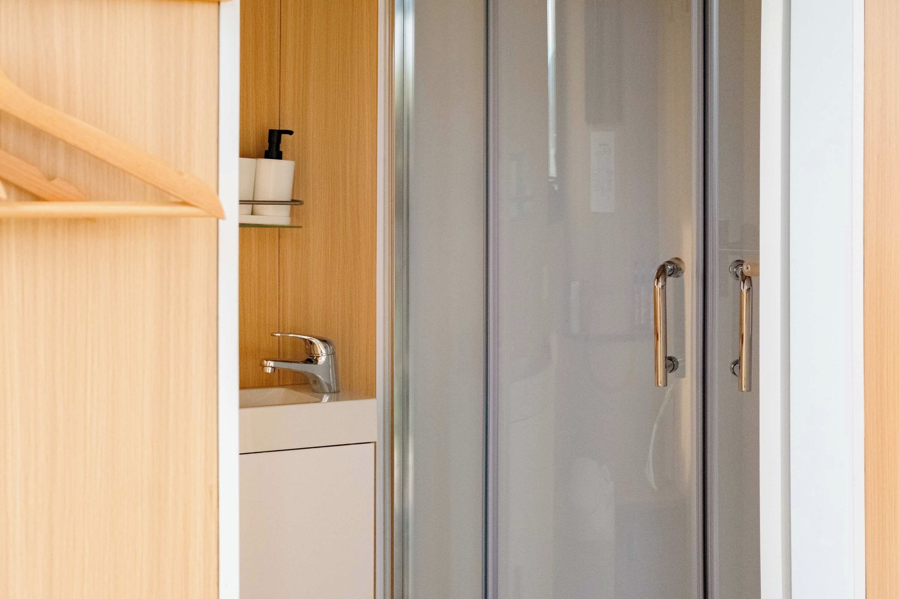 Une salle de bain moderne avec une douche à l’italienne en verre, un meuble-lavabo en bois et un lavabo blanc.
