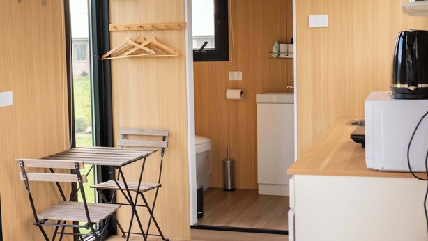 Une cuisine compacte avec des meubles en bois, un plan de travail blanc, une machine à café et un étendoir à vêtements suspendu.