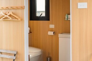 Een kleine badkamer met toilet, een klein raam, een houten wand en een plank met toiletartikelen.