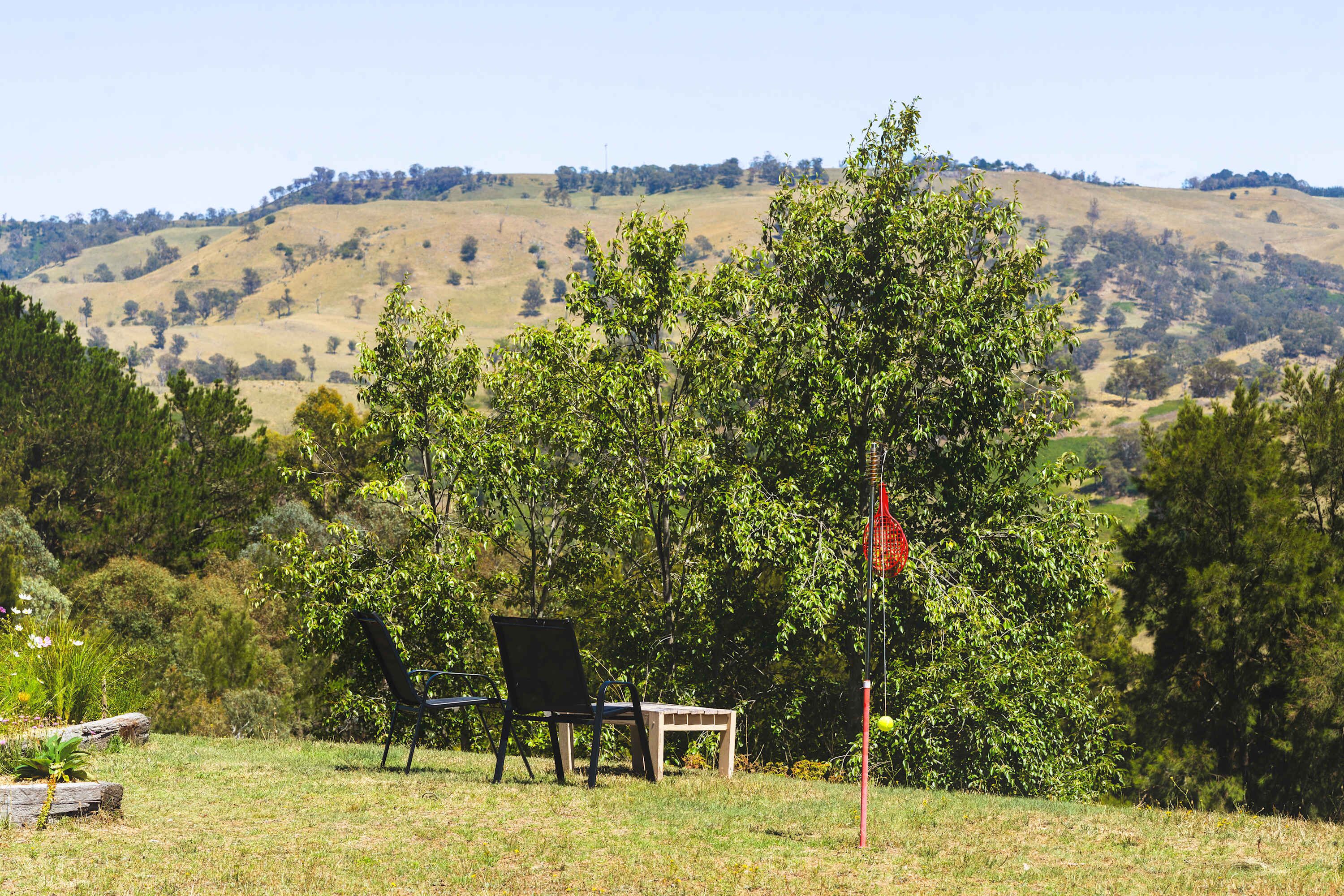 A grassy outdoor area with a chair and a small table, surrounded by trees and hills in the background.