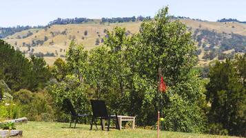 A grassy outdoor area with a chair and a small table, surrounded by trees and hills in the background.