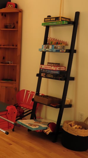 Una habitación con una estantería de madera, una silla roja y una pequeña mesa con un juguete rojo.
