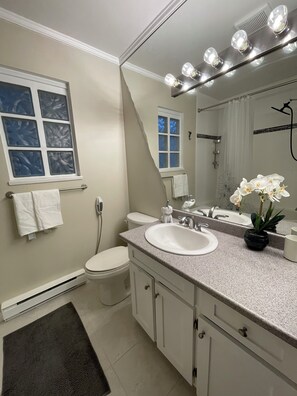 Un baño moderno con tocador blanco, un espejo grande y zona de ducha.