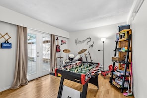 A room with a foosball table, a drum set, and a guitar on the wall.