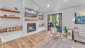 A modern living room with a fireplace, wooden shelves, a large window, and a cozy seating area. - Bright Tahoe Home w/ Private Backyard, Near Beach (Tahoe City)