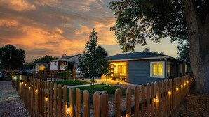 A residential property with a wooden fence, a well-lit front yard, and a house with a visible porch and windows. - The Mile High Haven: An Entertainers Dream Home with Hot Tub + Perfect Location (Lakewood)