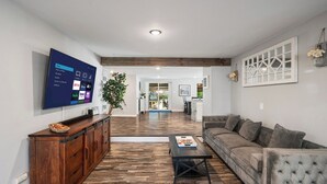 A modern living room with a flat-screen TV, wooden flooring, a grey sofa, and a coffee table. - The Mile High Haven: An Entertainers Dream Home with Hot Tub + Perfect Location (Lakewood)