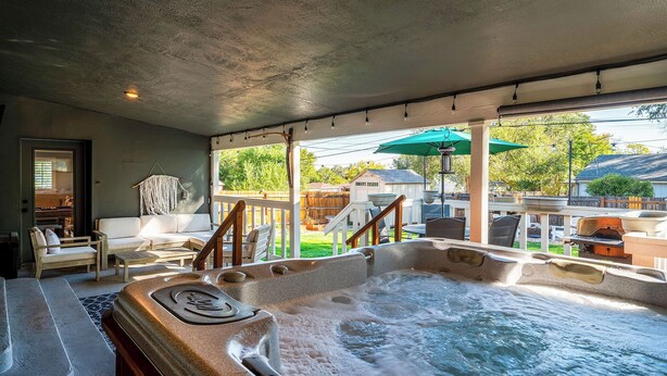 A hot tub area with a wooden deck, outdoor seating, and a view of the backyard. - The Mile High Haven: An Entertainers Dream Home with Hot Tub + Perfect Location (Lakewood)
