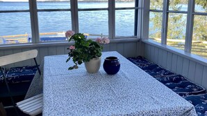 Une pièce dotée d’une grande fenêtre donnant sur un plan d’eau, d’une table ornée d’un vase de fleurs et d’un banc agrémenté de coussins à motifs floraux.