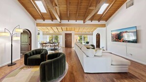 A spacious living room with a wooden ceiling, a large sofa, a floor lamp, and a painting on the wall. - Villa Sol: Private Las Palmas Estate Home (Palm Springs)