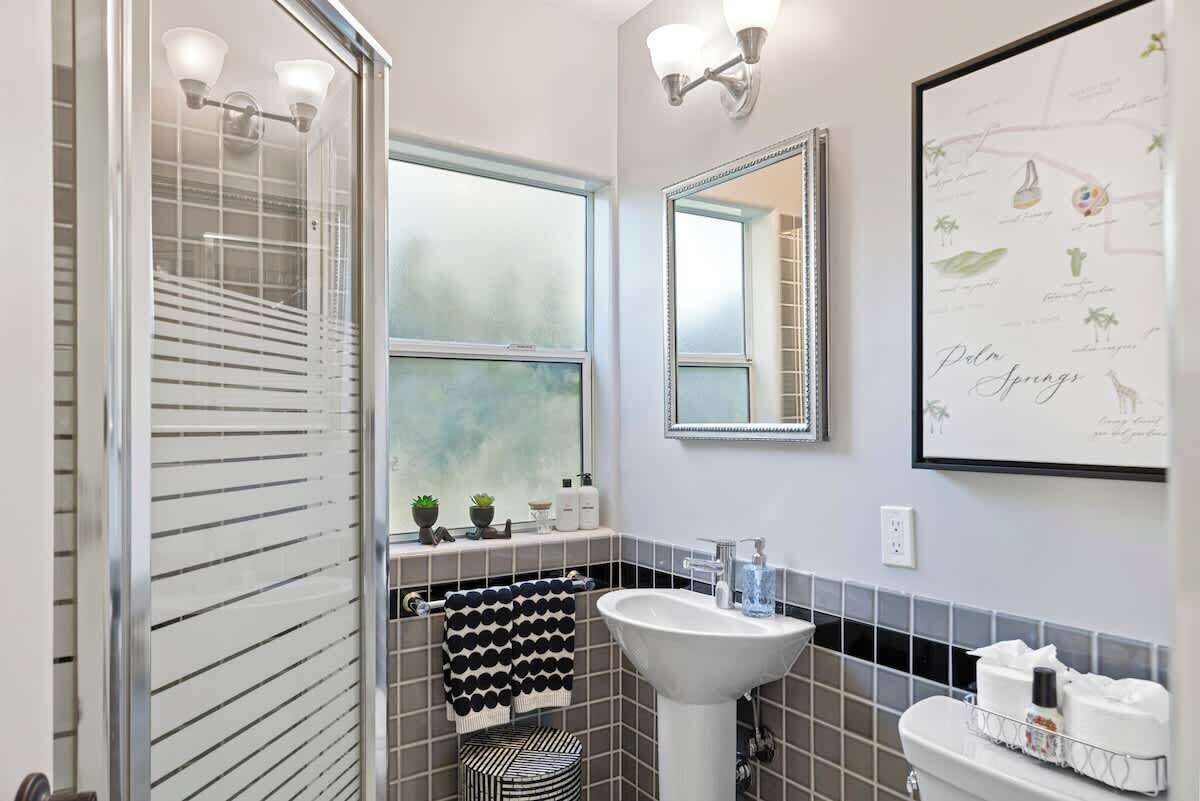 Un bagno con un lavandino bianco, uno specchio, un portascopevoli e una finestra con persiane.