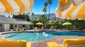 A swimming pool with yellow and white striped umbrellas, yellow lounge chairs, and a view of palm trees and mountains. - Villa Sol: Private Las Palmas Estate Home (Palm Springs)