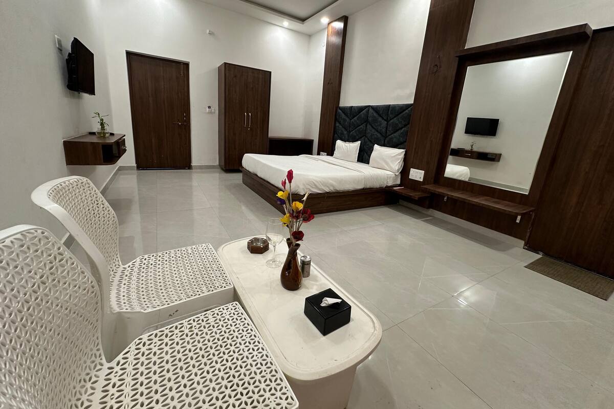 A modern hotel room with a bed, a desk with a vase of flowers, a chair, and a TV mounted on the wall.