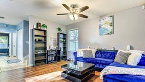 A modern living room with a blue sofa set, a coffee table, and a ceiling fan. - Spacious 3BR Two-Story Home Near Downtown Jax (Jacksonville)