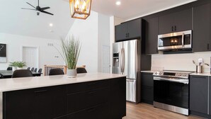 A modern kitchen with a central island, stainless steel appliances, and a ceiling fan.