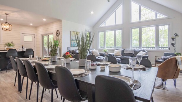 A spacious living area with a dining table set for six, a large window with a view of trees, and a ceiling fan.