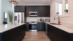 A modern kitchen with dark cabinets, stainless steel appliances, and a wooden floor.