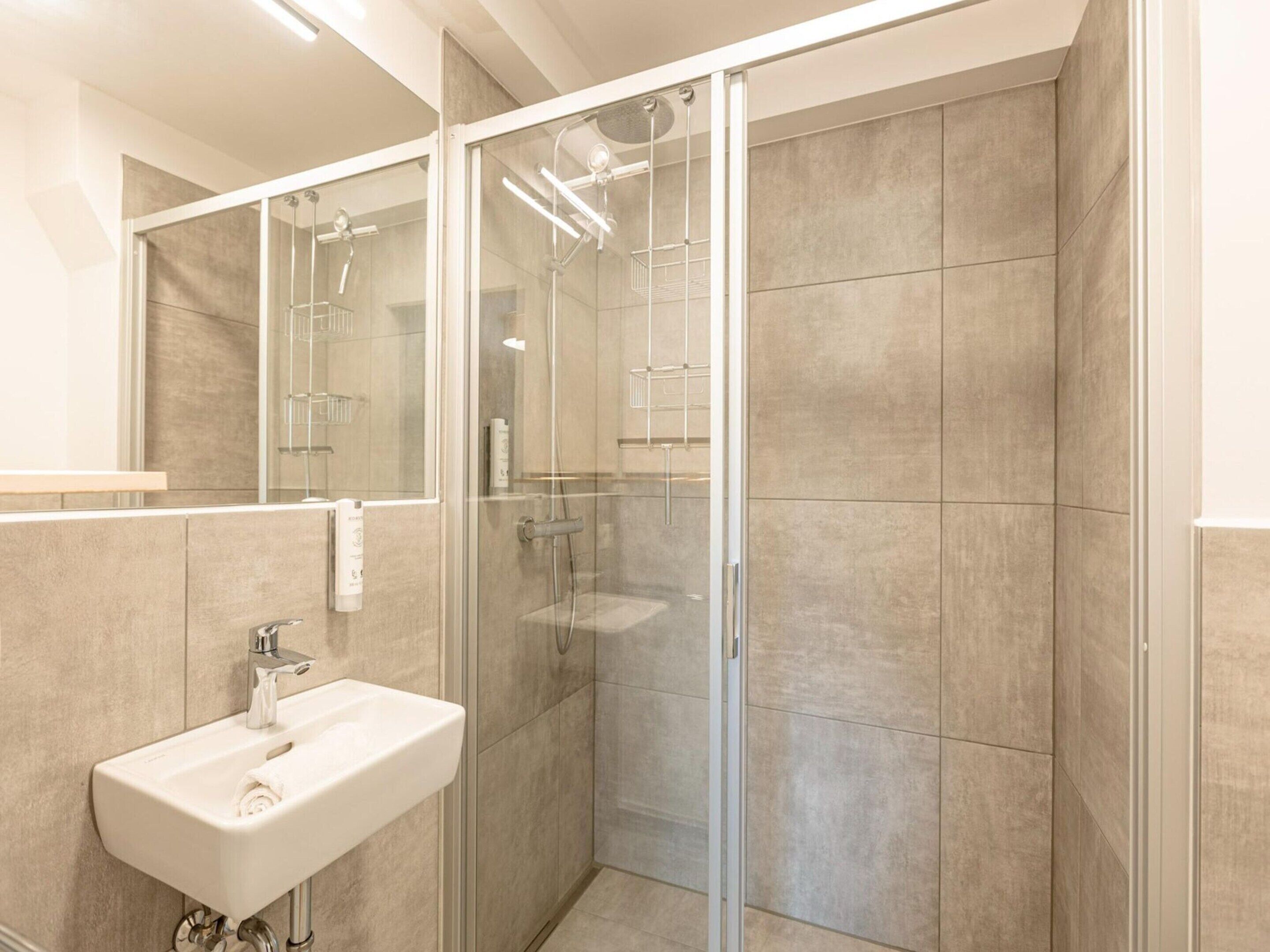 Ein modernes Badezimmer mit einer Duschkabine aus Glas, einem weißen Waschbecken und gefliesten Wänden.