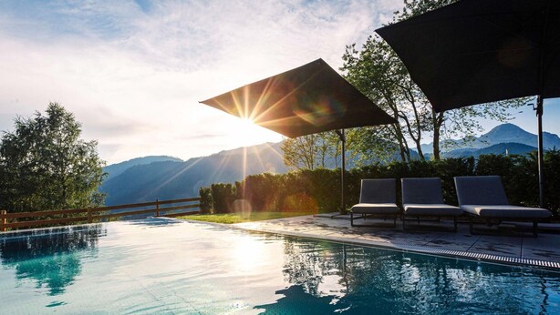 Une piscine avec vue sur les montagnes, des chaises longues et une clôture en bois.