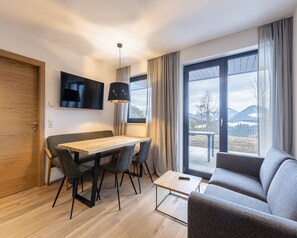 Ein modernes Wohnzimmer mit einem Holzespeisetisch, einem grauen Sofa und einem an der Wand befestigten Fernseher.