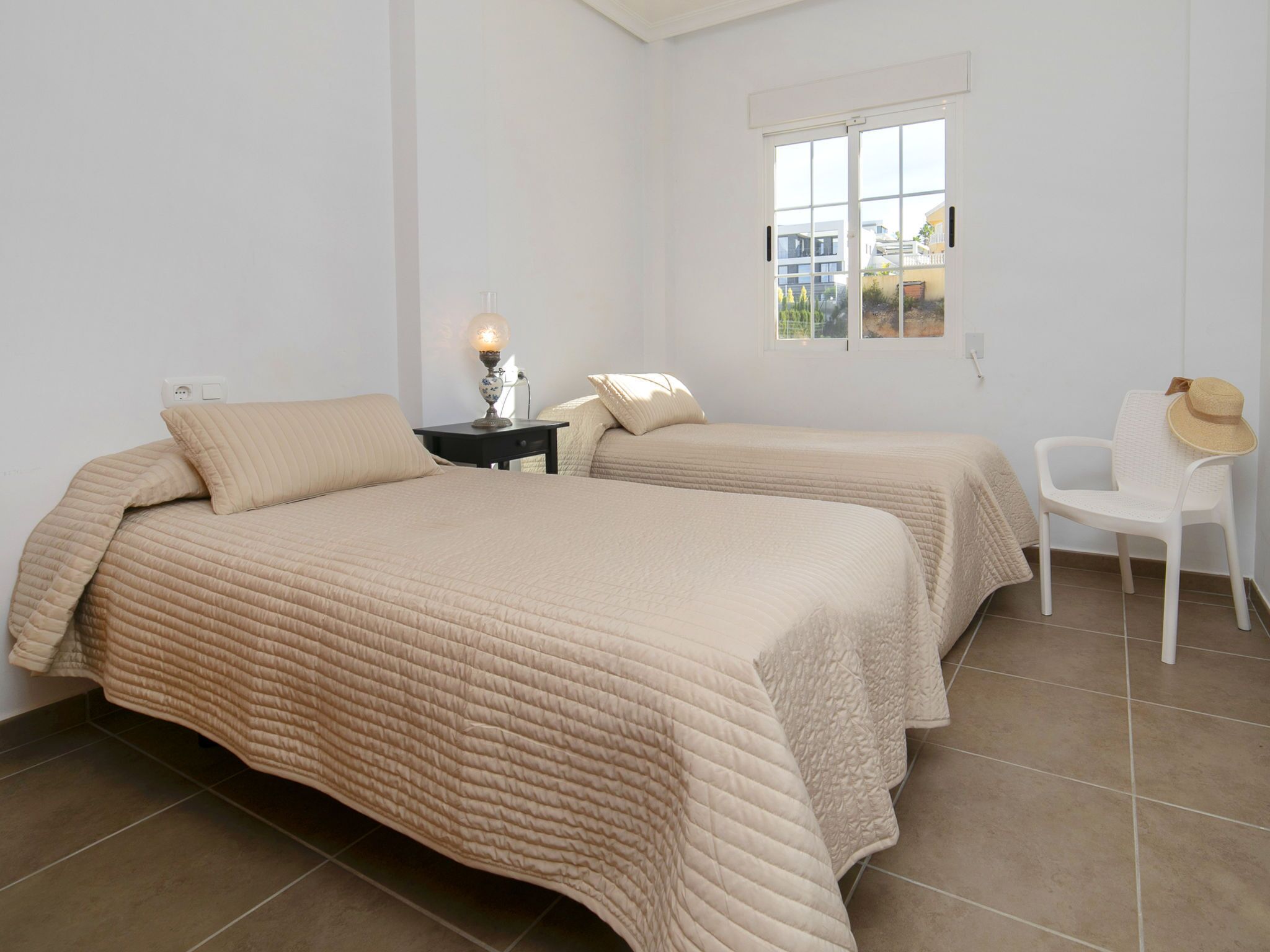 A bedroom with two beds, a nightstand, a lamp, a chair, and a window.