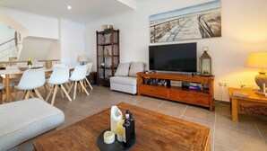 Un salon moderne dot é d’un téléviseur à écran plat, d’une table basse en bois, d’une bibliothèque et d’un coin repas avec des chaises et une table.