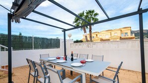 Une terrasse extérieure avec une table dressée pour le repas, des chaises et une vue sur un bâtiment jaune et des palmiers.