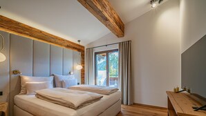 Ein modernes Schlafzimmer mit einem großen Bett, Holzbalkendecke und Blick ins Freie.