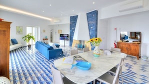 Un moderno vestíbulo de hotel con suelo de baldosas azules y blancas, un mostrador de recepción de mármol, un sofá azul y un televisor.